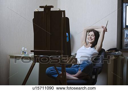 Stock Image - Woman sitting in front of easel smiling. Fotosearch
