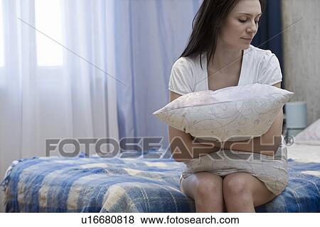 Stock Photo - Woman sitting on bed and hugging pillow. Fotosearch