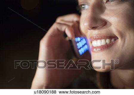 Woman smiles as she listens on mobile phone at night View Large Photo Image Stock Photo - Woman smiles as she listens on mobile phone at night. Fotosearch