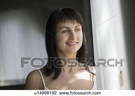 Woman standing near window in natural light View Large Photo Image Stock Image - Woman standing near window in natural light. Fotosearch