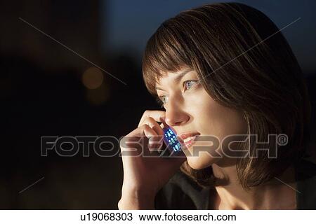 Stock Image - Woman talks on mobile phone at night. Fotosearch