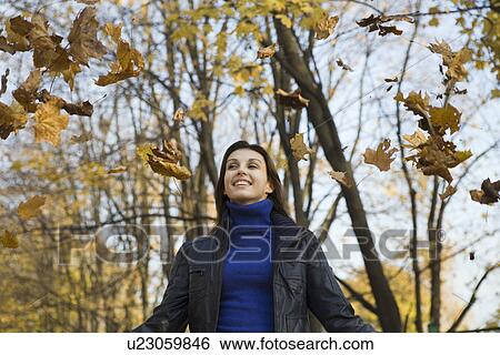 Woman under falling leaves in park View Large Photo Image Stock Photograph - Woman under falling leaves in park. Fotosearch