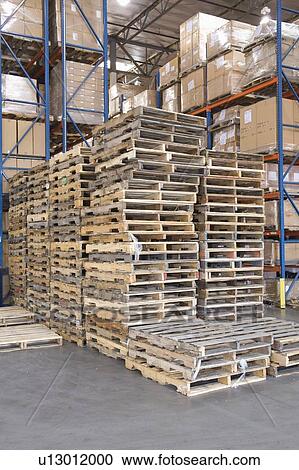 Stock Image - Wooden pallets stacked in distribution warehouse. Fotosearch