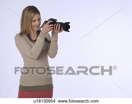 Picture - Young (20-25 years) female photographer holding camera studio shot. Fotosearch