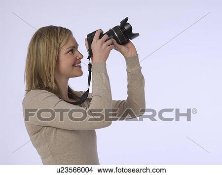 Picture - Young (20-25 years) female photographer holding camera studio shot. Fotosearch