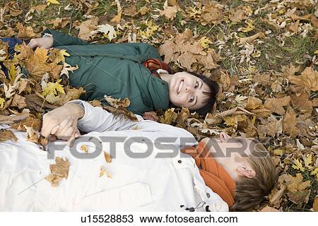 Stock Image - Young couple lying on leaves in park. Fotosearch