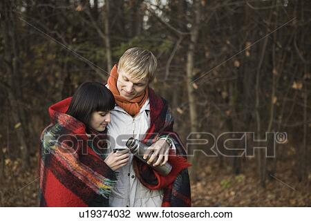 Stock Image - Young couple wrapped in blanket embracing in forest. Fotosearch