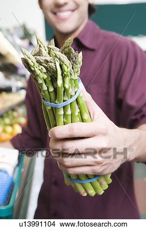 Young man holding asparagus in supermarket View Large Photo Image Picture - Young man holding asparagus in supermarket. Fotosearch