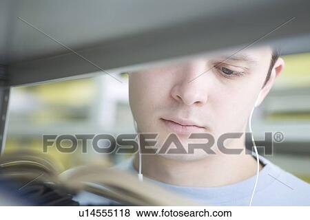 Stock Photo - Young man reading in library view through shelf. Fotosearch