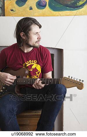 Young man sits playing electric guitar View Large Photo Image Stock Image - Young man sits playing electric guitar. Fotosearch