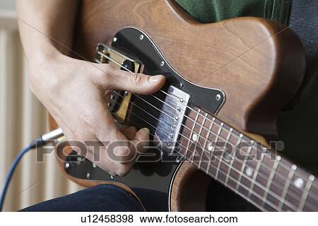 Young man strums chord on guitar View Large Photo Image Stock Photo - Young man strums chord on guitar. Fotosearch