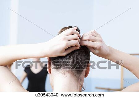 Stock Image - Young woman adjusts hair during ballet class. Fotosearch
