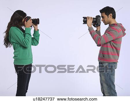 Stock Photo - Young woman and young man photographing each other studio shot. Fotosearch