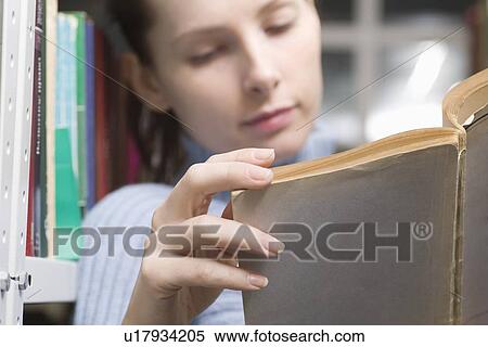 Stock Photography - Young woman reads book in library. Fotosearch