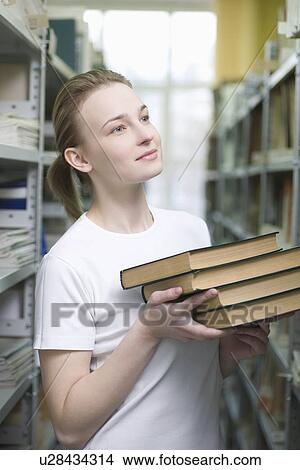 Picture - Young woman returns library books to shelves. Fotosearch