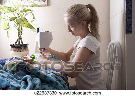Stock Image - Young woman sits making patchwork at sewing machine. Fotosearch