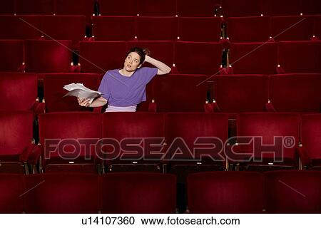 Stock Image - Young woman sitting in theatre stalls. Fotosearch