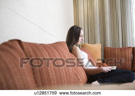 Stock Photo - Young woman sitting on sofa and reading book portrait. Fotosearch