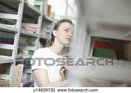 Young woman stands at library shelving View Large Photo Image Stock Image - Young woman stands at library shelving. Fotosearch