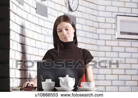 Stock Image - Young woman using laptop in cafe. Fotosearch