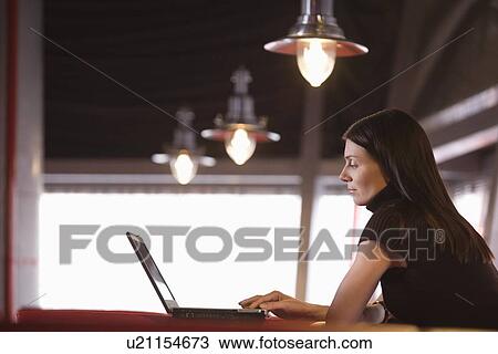 Stock Image - Young woman using laptop in cafe. Fotosearch
