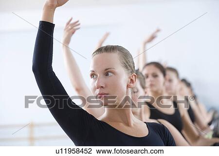 Stock Image - Young women with arms raised at the barre. Fotosearch