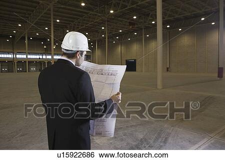 Man studies blueprint in empty warehouse View Large Photo Image Stock Photograph - Man studies blueprint in empty warehouse. Fotosearch