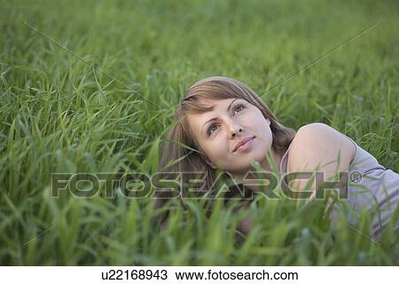 Young woman lies in a field of grass, looking up View Large Photo Image Stock Image - Young woman lies in a field of grass, looking up. Fotosearch