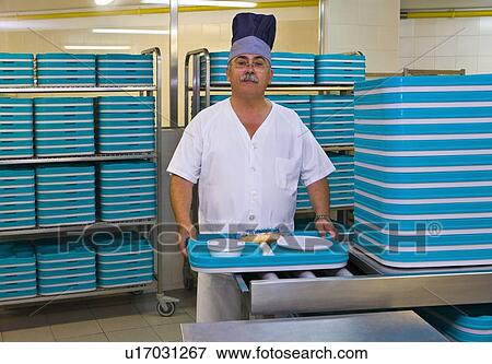 Stock Photo - Chef stands in hospital kitchen with plastic trays. Fotosearch