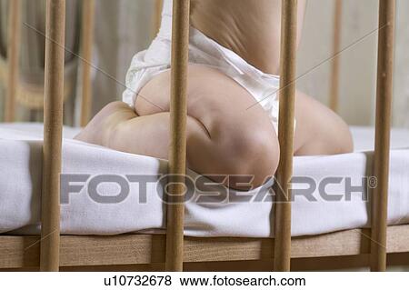 Stock Photo - INfant child kneeling in cot. Fotosearch