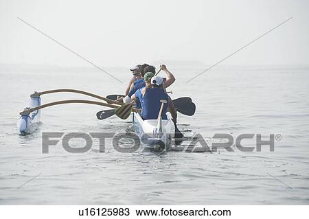 Stock Image - Outrigger canoeing team on water. Fotosearch