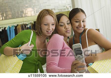 Stock Photography - 3 Girl friends Posing for Camera Phone Picture in clothing store. Fotosearch