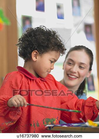 Art teacher squatting next to boy painting in art class View Large Photo Image Stock Image - Art teacher squatting next to boy painting in art class. Fotosearch