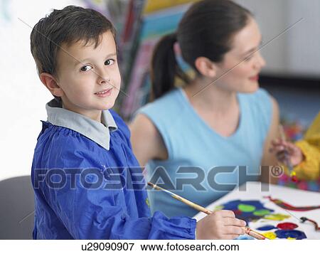 Stock Photo - Art teacher squatting next to boy painting in art class. Fotosearch