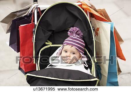 Stock Photography - Baby sitting in stroller hung with shopping bags, outdoors. Fotosearch
