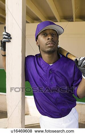 Stock Photo - Baseball player holding bat in dugout, (portrait). Fotosearch