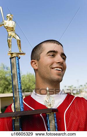 Stock Photo - Baseball player holding trophy on field. Fotosearch