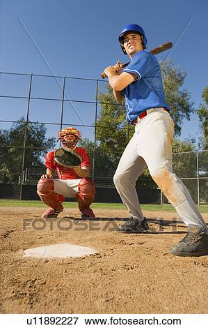 Stock Photo - Baseball player swinging baseball bat, catcher crouching in background. Fotosearch