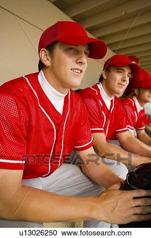 Stock Image - Baseball team-mates sitting in dugout. Fotosearch