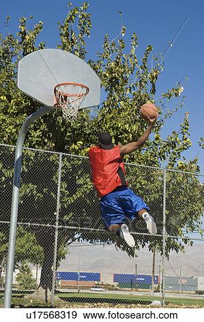 Stock Photo - Basketball player, mid-air, shooting ball, back view. Fotosearch
