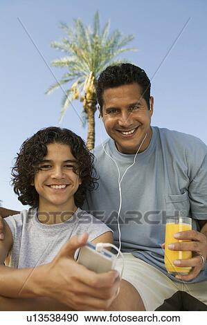 Boy (13-15) holding portable music player, father listening with earphones an holding glass of juice, front view portrait. View Large Photo Image Stock Image - Boy (13-15) holding portable music player, father listening with earphones an holding glass of juice, front view portrait.. Fotosearch