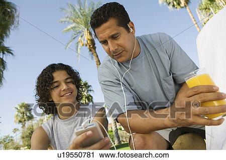 Boy (13-15) holding portable music player, father listening with earphones and holding glass of juice. View Large Photo Image Stock Image - Boy (13-15) holding portable music player, father listening with earphones and holding glass of juice.. Fotosearch