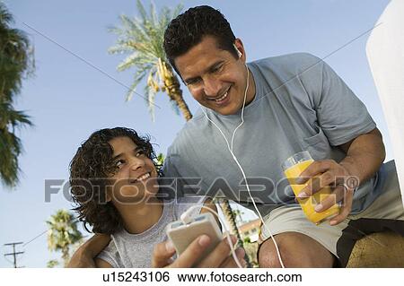 Boy (13-15) holding portable music player, father listening with earphones and holding glass of juice. View Large Photo Image Stock Photograph - Boy (13-15) holding portable music player, father listening with earphones and holding glass of juice.. Fotosearch