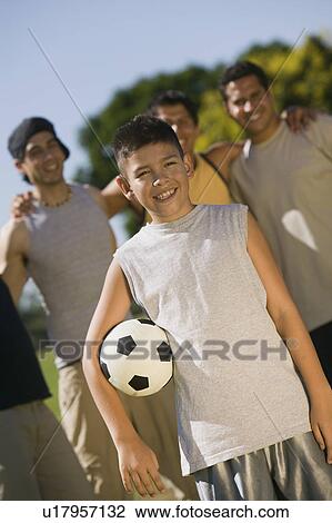 Stock Image - Boy (13-15) holding soccer ball, with four men at park.. Fotosearch