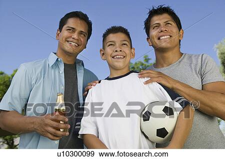 Boy (13-15) holding soccer ball with two brothers outdoors, front low angle view. View Large Photo Image Stock Photo - Boy (13-15) holding soccer ball with two brothers outdoors, front low angle view.. Fotosearch