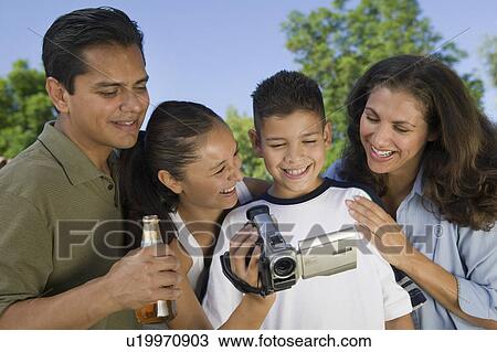 Stock Image - Boy (13-15) looking at camcorder with family, outdoors.. Fotosearch