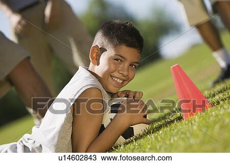 Boy (13-15) lying down on grass, holding soccer ball. View Large Photo Image Stock Image - Boy (13-15) lying down on grass, holding soccer ball.. Fotosearch