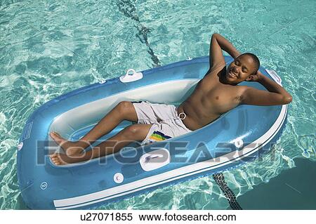 Stock Photography - Boy (13-15) Relaxing on Inflatable Raft in swimming pool, elevated view.. Fotosearch