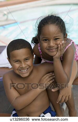 Stock Photograph - Boy (7-9) and girl (5-6) sitting by swimming pool, portrait.. Fotosearch