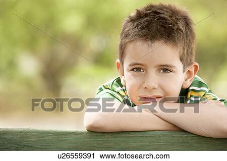 Stock Image - Boy (7-9) leaning against railing, front view portrait.. Fotosearch
